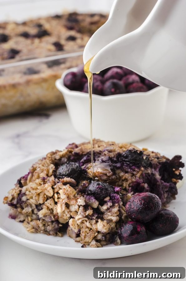 A piece of banana blueberry baked oats on a plate with maple syrup being drizzled over the top.