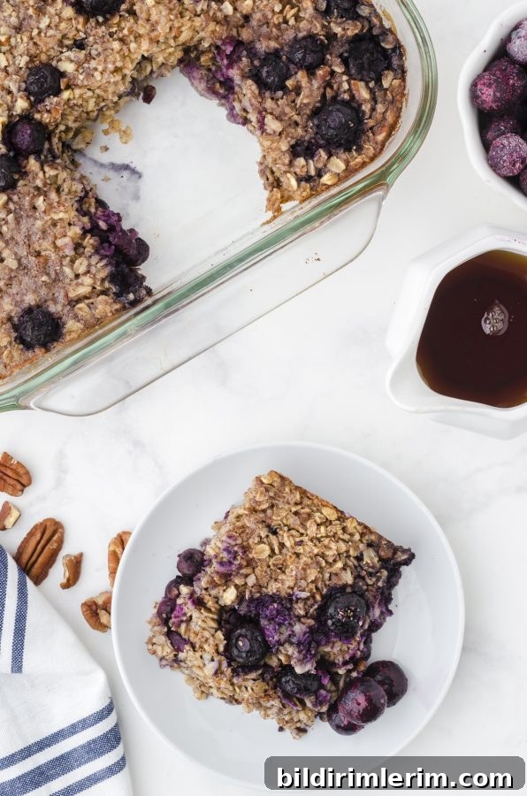 A slice of baked oats with bananas and blueberries on a serving plate with the pan of baked oats behind it.