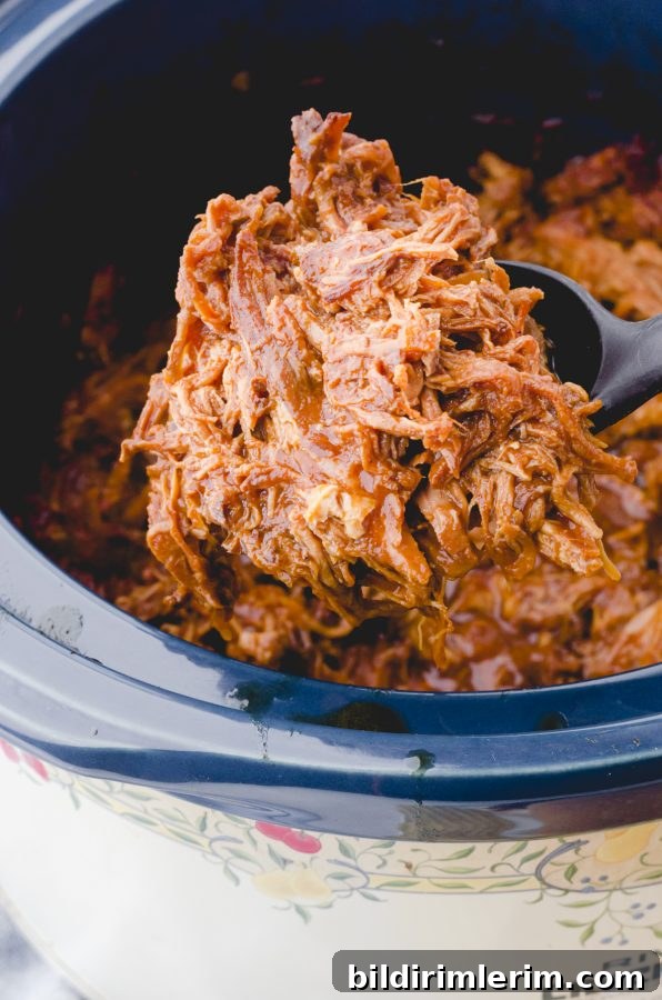 Crock Pot Pulled Pork Recipe: Tender, Juicy BBQ Flavor 7 A serving spoon dishing out pulled pork in crock pot.
