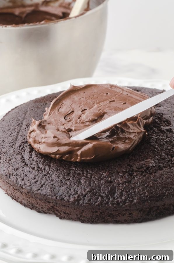 A frozen chocolate cake layer with chocolate frosting being spread on top