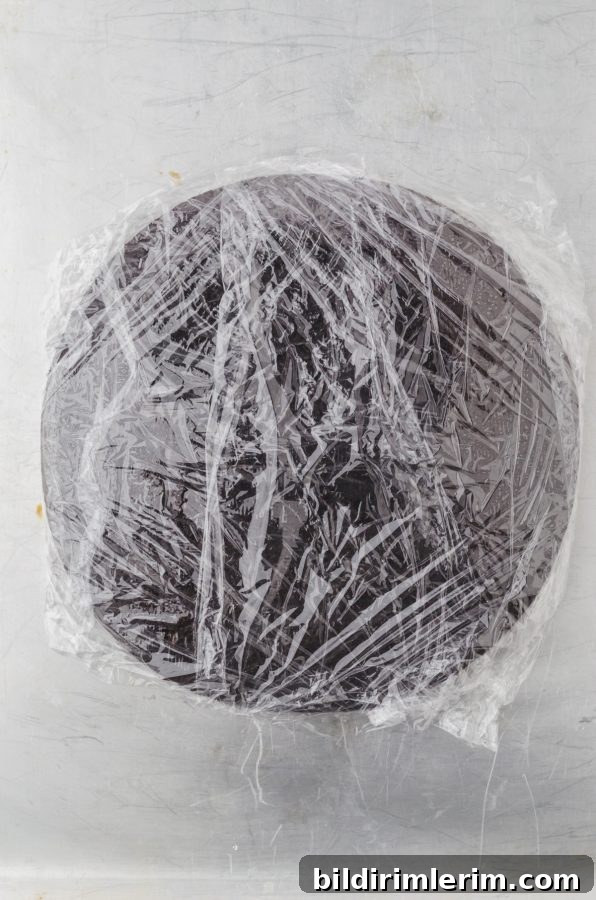 A chocolate cake layer wrapped in plastic wrap ready to go in the freezer
