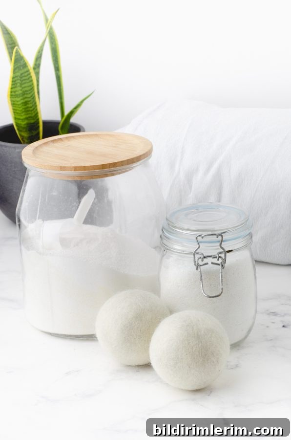 Large glass jar with laundry detergent powder and two wool dryer balls beside it.