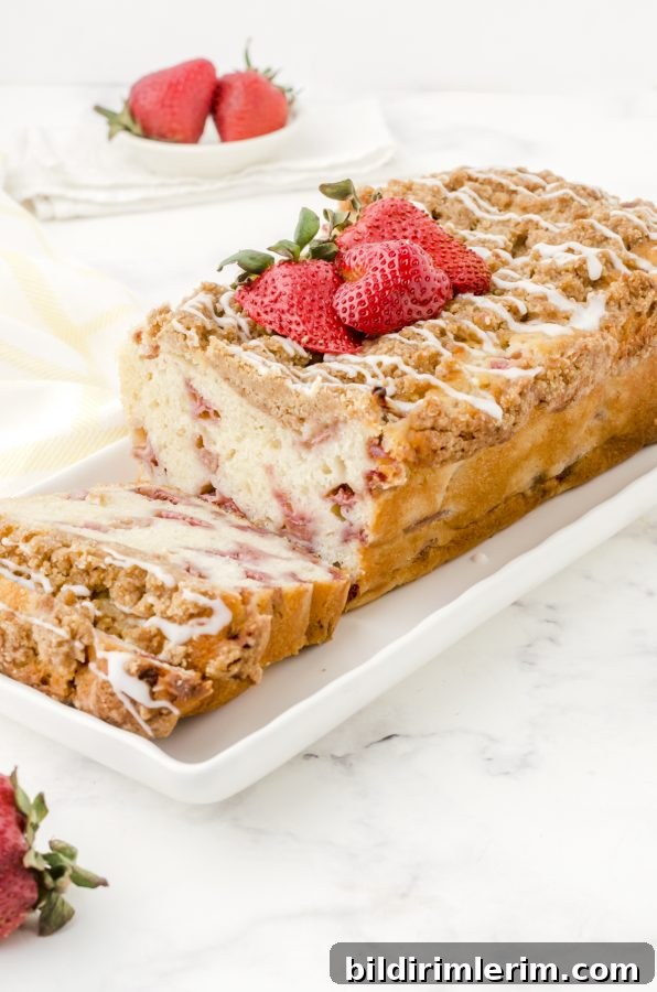 Strawberry bread with crumble topping and vanilla glaze on a white serving platter.