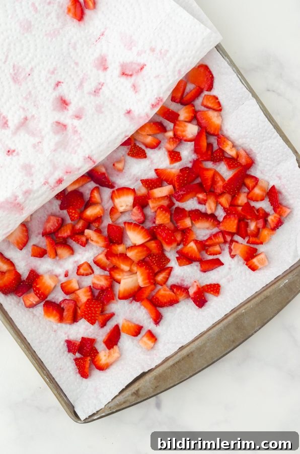 Cut up strawberries sitting on a paper towel in a large baking sheet