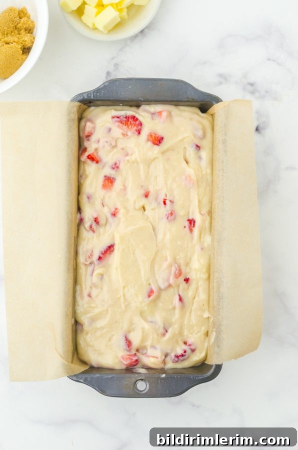 A loaf pan lined with parchment paper filled with strawberry quick bread batter.