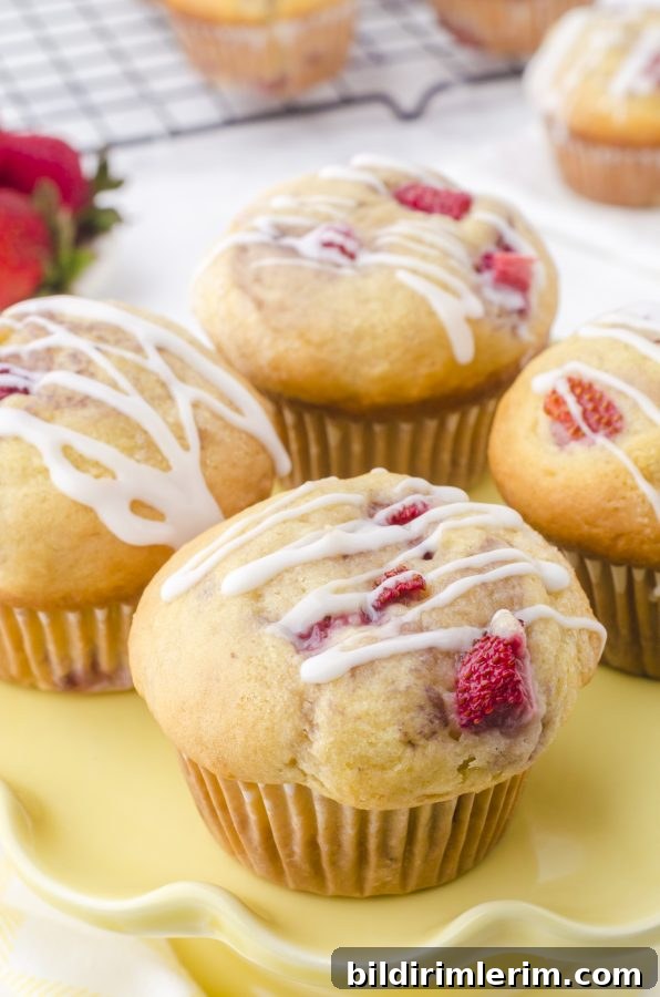 Buttermilk strawberry muffins on a yellow serving dish with vanilla glaze drizzled on the tops.