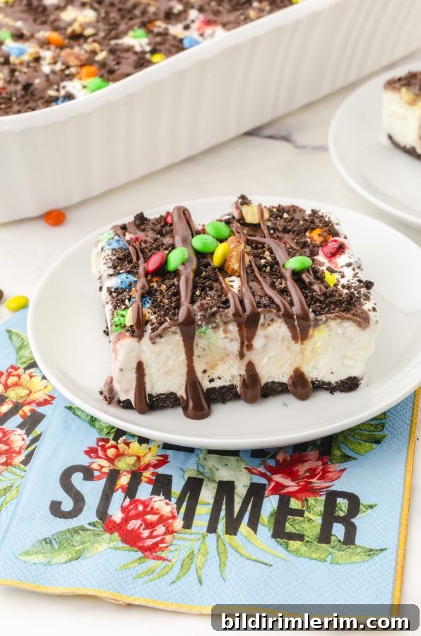How to Make Oreo Ice Cream Cake with Oreo Crust 8 Oreo ice cream cake on a dessert plate drizzled with hot fudge sauce and a sprinkle of m&ms on the top