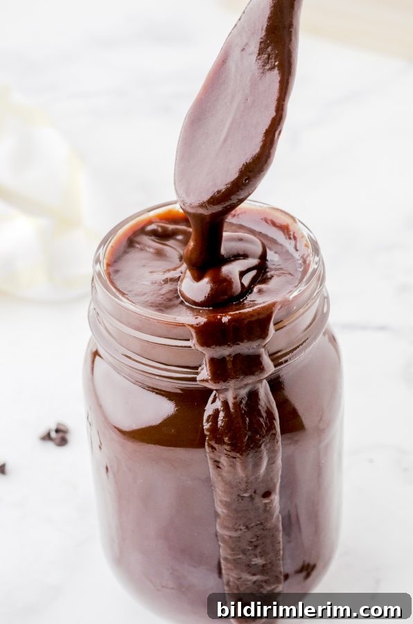 Homemade chocolate fudge sauce (hot fudge sauce) in a mason jar with a spoon drizzling the thick mixture into the top.