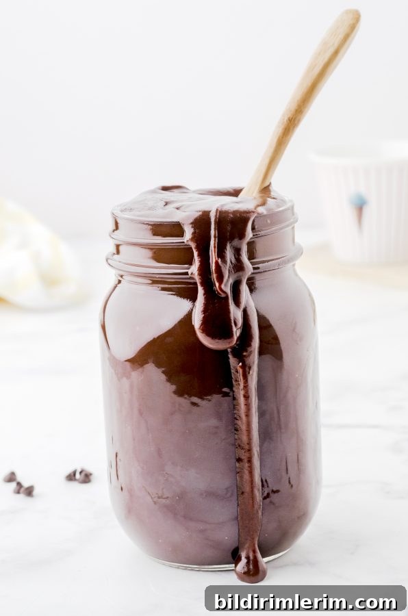 Homemade chocolate fudge sauce in a jar with a spoon in it