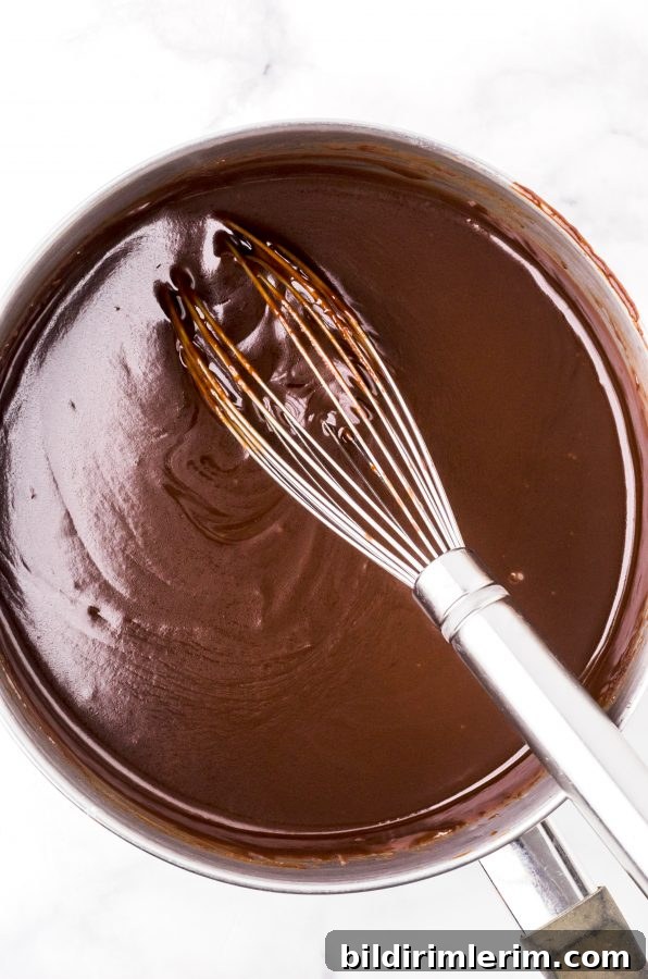 Finished homemade hot fudge sauce in a saucepan with a whisk sitting in it.