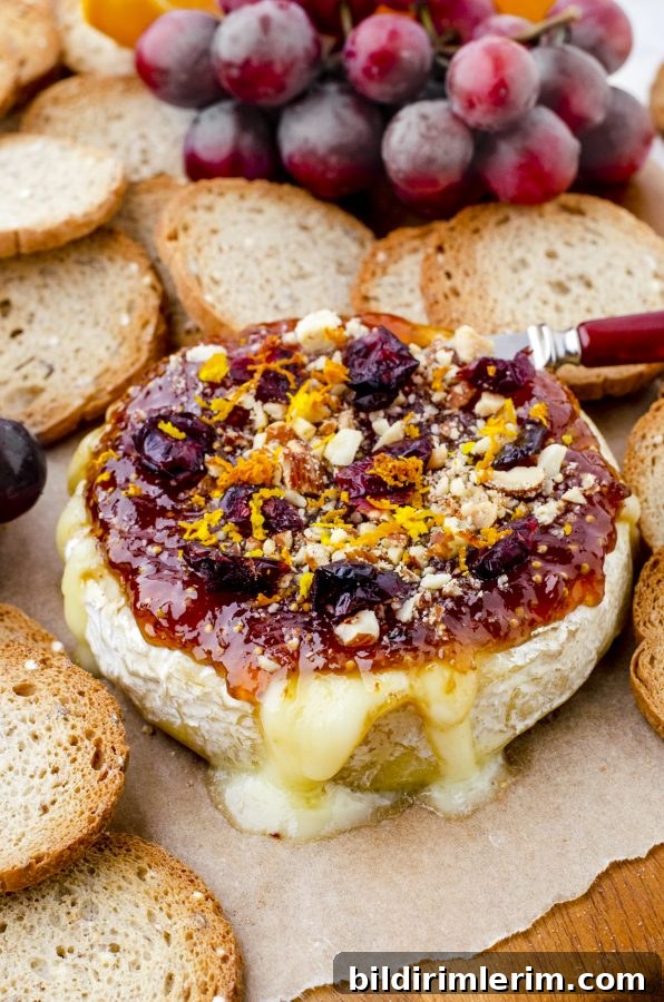 baked brie on a charcuterie board with crackers and grapes behind it