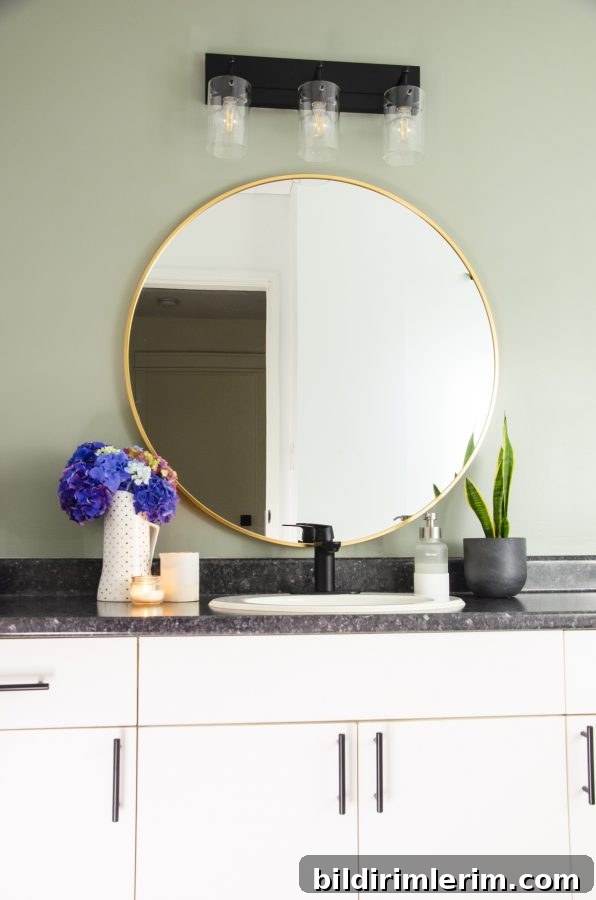 Evergreen Fog Bathroom Remodel: Affordable Paint and Design Ideas 5 The vanity area with a round mirror with brass frame and new light fixtures, and the wall painted in evergreen fog by Sherwin Williams.