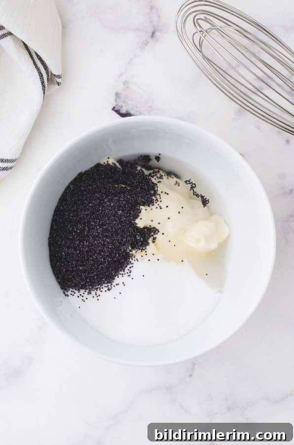 Ingredients for creamy poppyseed dressing in a bowl with a whisk beside it.