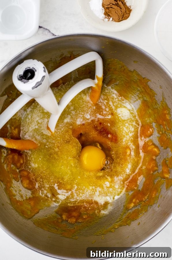 Pumpkin Banana Muffins Recipe with Cinnamon 5 An egg, butter and vanilla that has been added to the pumpkin mixture in the bowl of an electric mixer for banana pumpkin muffins.