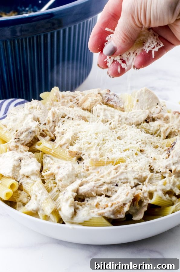 Slow cooker chicken alfredo in a serving bowl with cheese being sprinkled on the top.