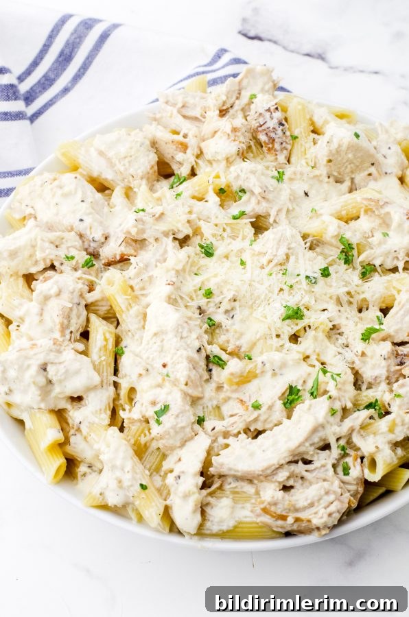 Crock pot chicken alfredo in a serving bowl poured over pasta.