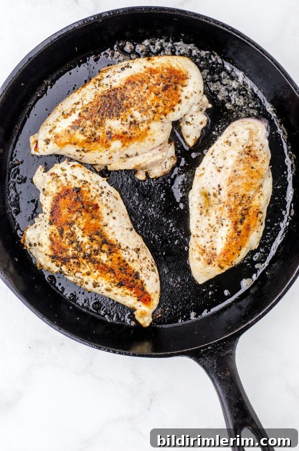 Chicken breasts being seared in a cast iron pan in preparation for being used for alfredo chicken in the crockpot