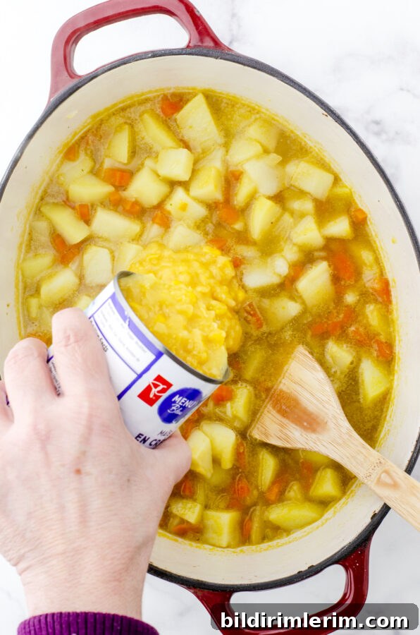 Creamed corn being added to the pot of potato soup.
