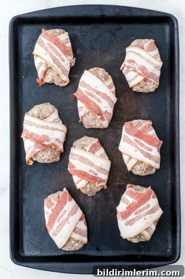 Bacon wrapped meatloaf in mini individual portions arranged on a baking pan ready to go into the oven.