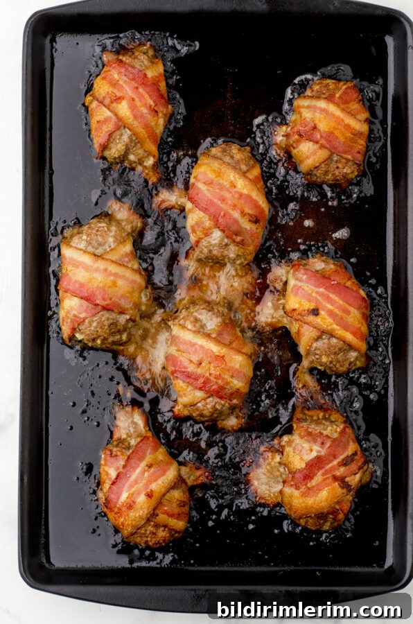 Baked mini bacon wrapped meatloaf portions on baking sheet right after being pulled from the oven.
