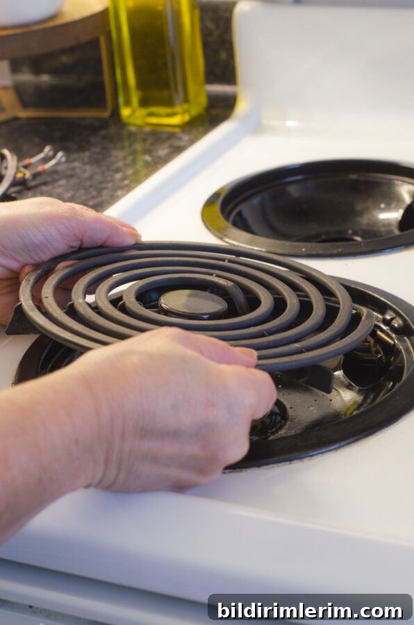 A woman removing the electric coil from a stovetop.