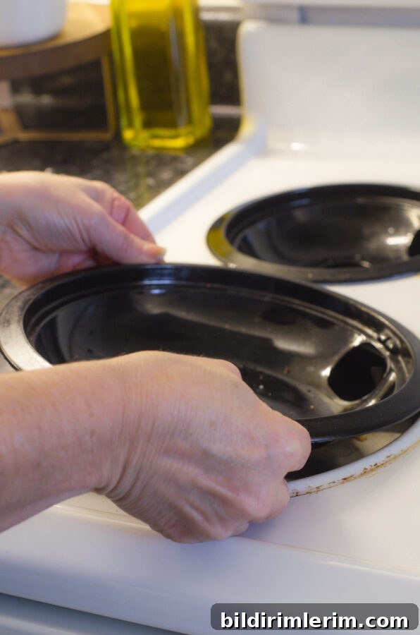 A woman removing the drip tray of an electric stovetop