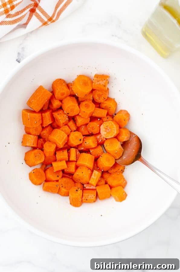 Carrots in a medium sized bowl being tossed with olive oil for sheet pan chicken and veggies recipe.