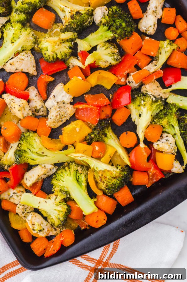 Close up of sheet pan chicken and veggies ingredients in a sheet pan - chicken, brocolli, peppers, and carrots.