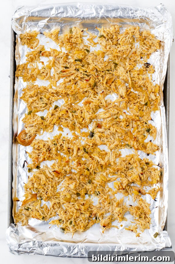 Crock pot shredded chicken on an aluminum foil covered baking sheet 