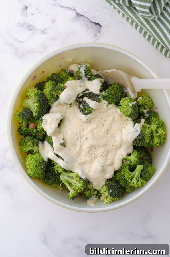 Classic Broccoli Salad with Cranberries Recipe 6 Dressing being mixed into a bowl of broccoli salad with cranberries and bacon