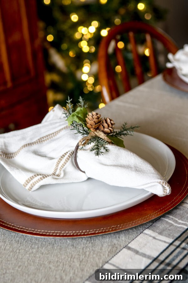 A leather charger plate with white plate on top and a cloth napkin with a napkin ring with pine cones on it.