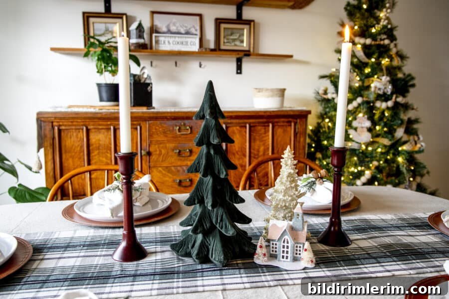 Christmas tablescape centerpiece with taper candles, trees, and a small village house.