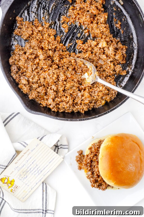 A pan of sloppy joes meat mixture with a sloppy joe in a bun on a plate in front of it.