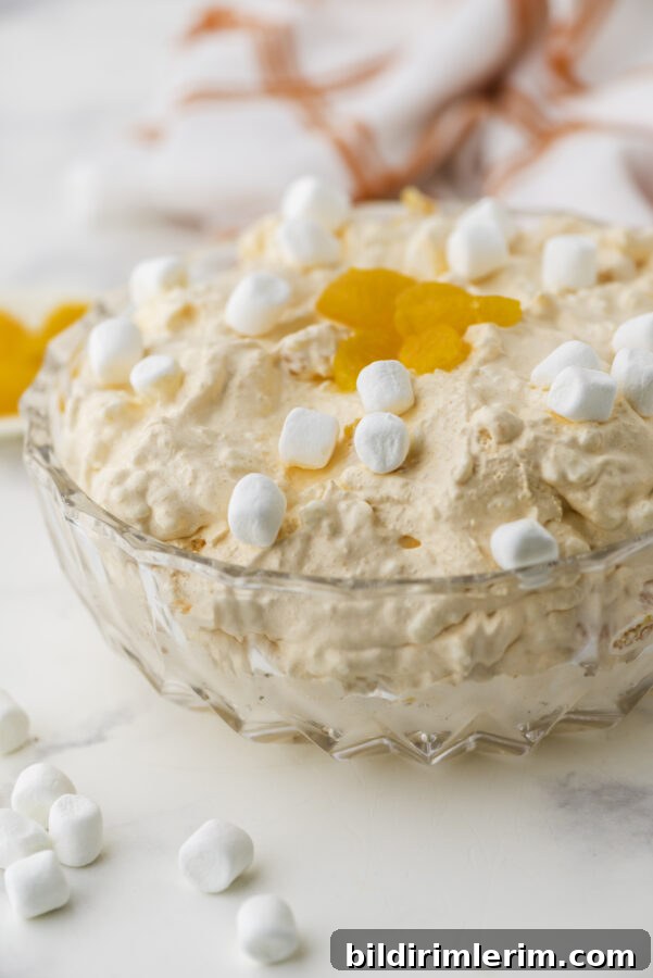 Classic orange fluff salad in a clear glass serving bowl with marshmallows and mandarin oranges garnishing the top.