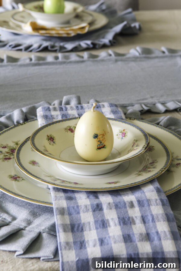 A table setting idea with a blue round ruffled placemat, blue and rose vintage china, blue checked cloth napkin, and a vintage egg candle sitting on the top of the top plate.