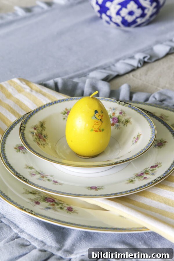 A table setting with vintage china, a yellow striped cloth napkin, and a yellow egg candle on the top plate.