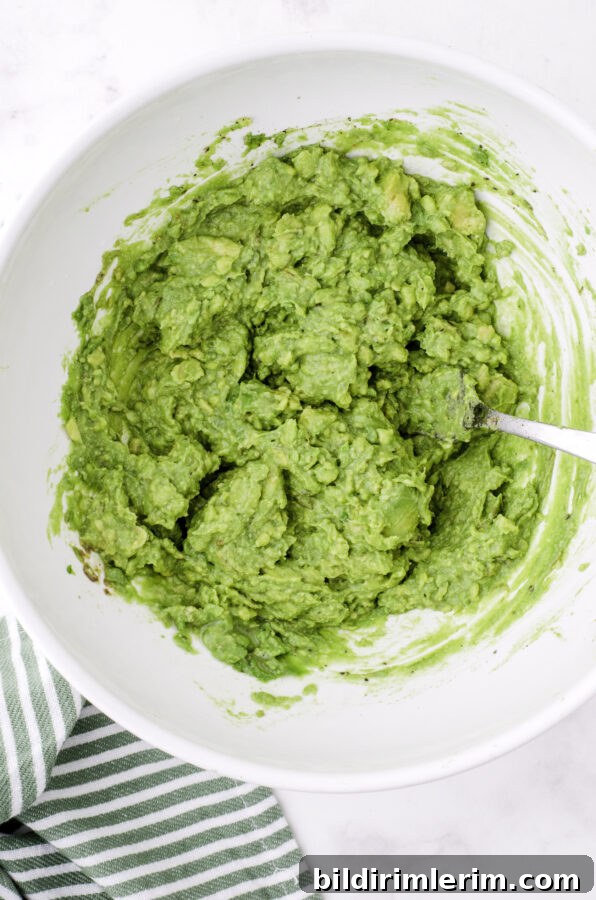 Mashed avocados with lemon juice and spices stirred together in a large bowl.