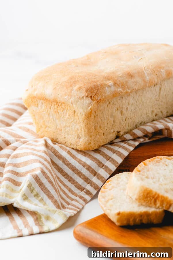A loaf of honey oat sourdough sandwich bread sitting on a striped cloth with a few slices beside it.
