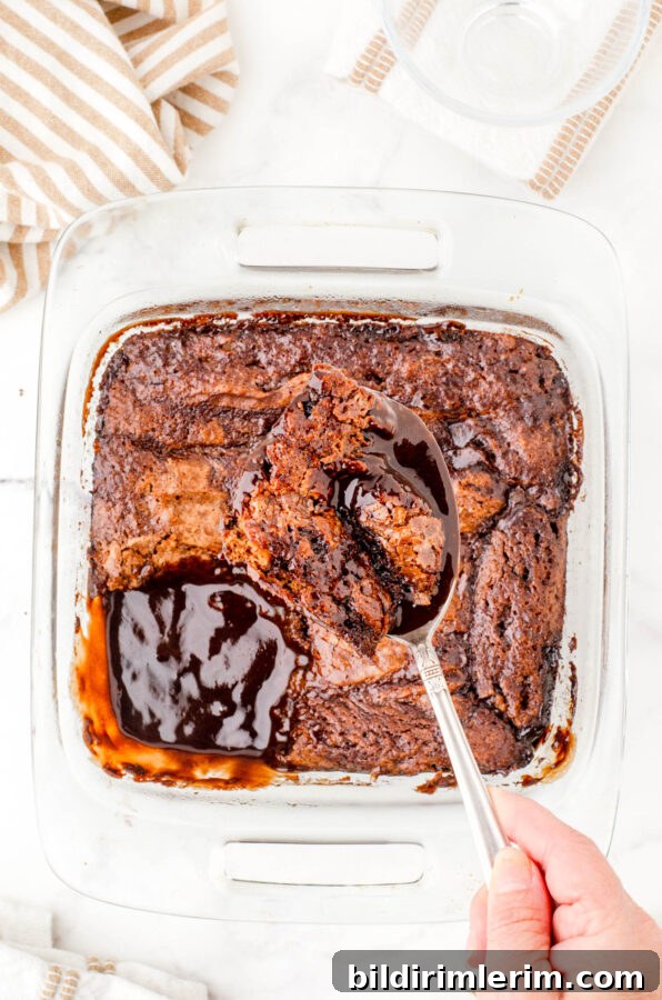 A scoop of hot fudge chocolate pudding cake being held above a pan of it showing how the cake and pudding are baked together.