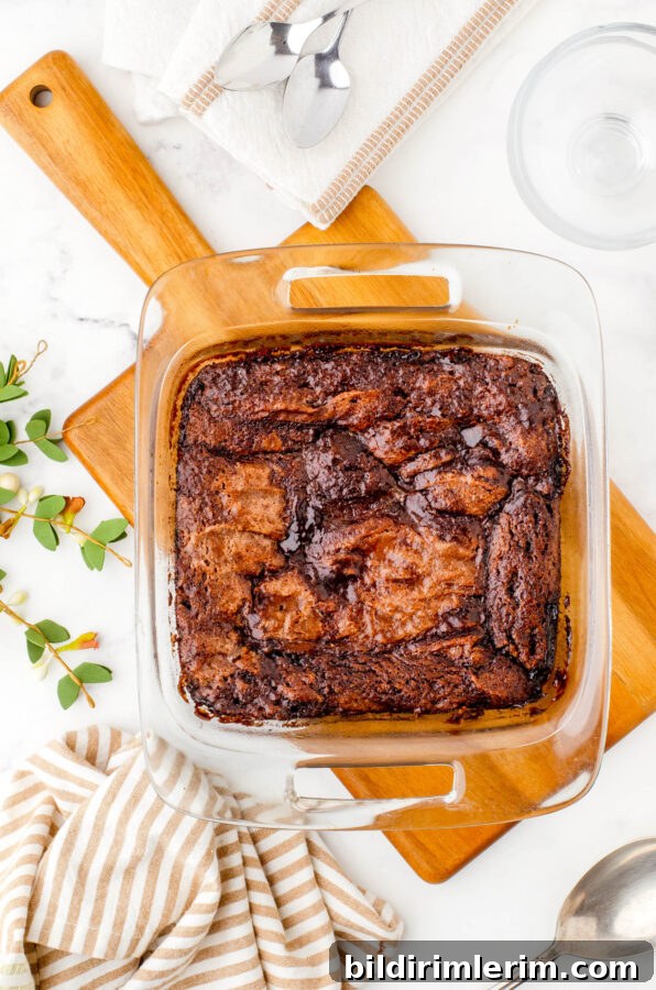 A pan of chocolate pudding cake baked and placed on a wooden cutting board while it cools.
