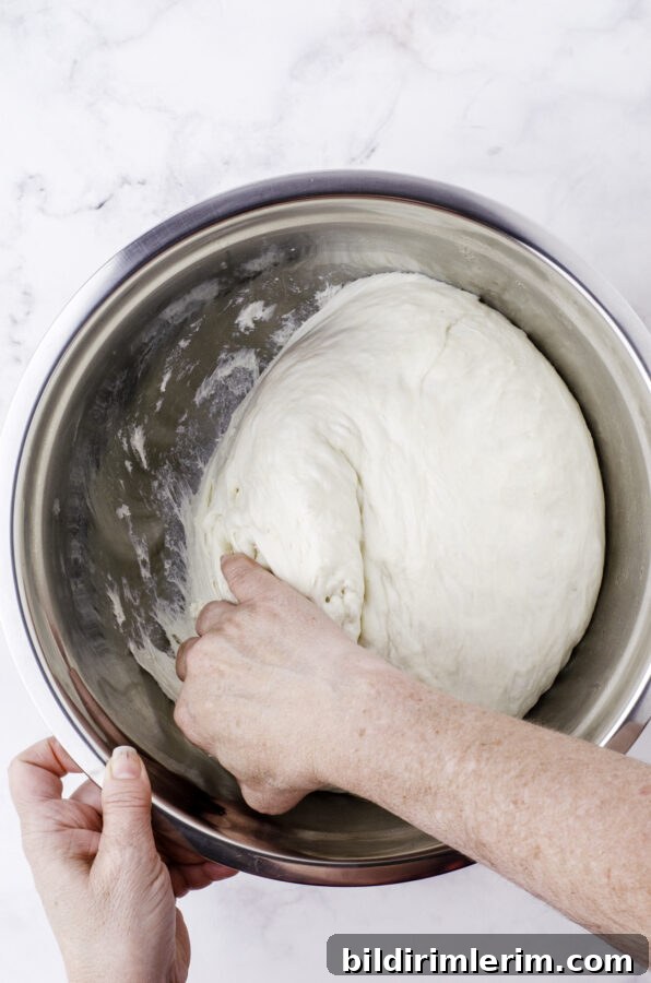 A woman pulling the sourdough dough away from the sides of the bowl.