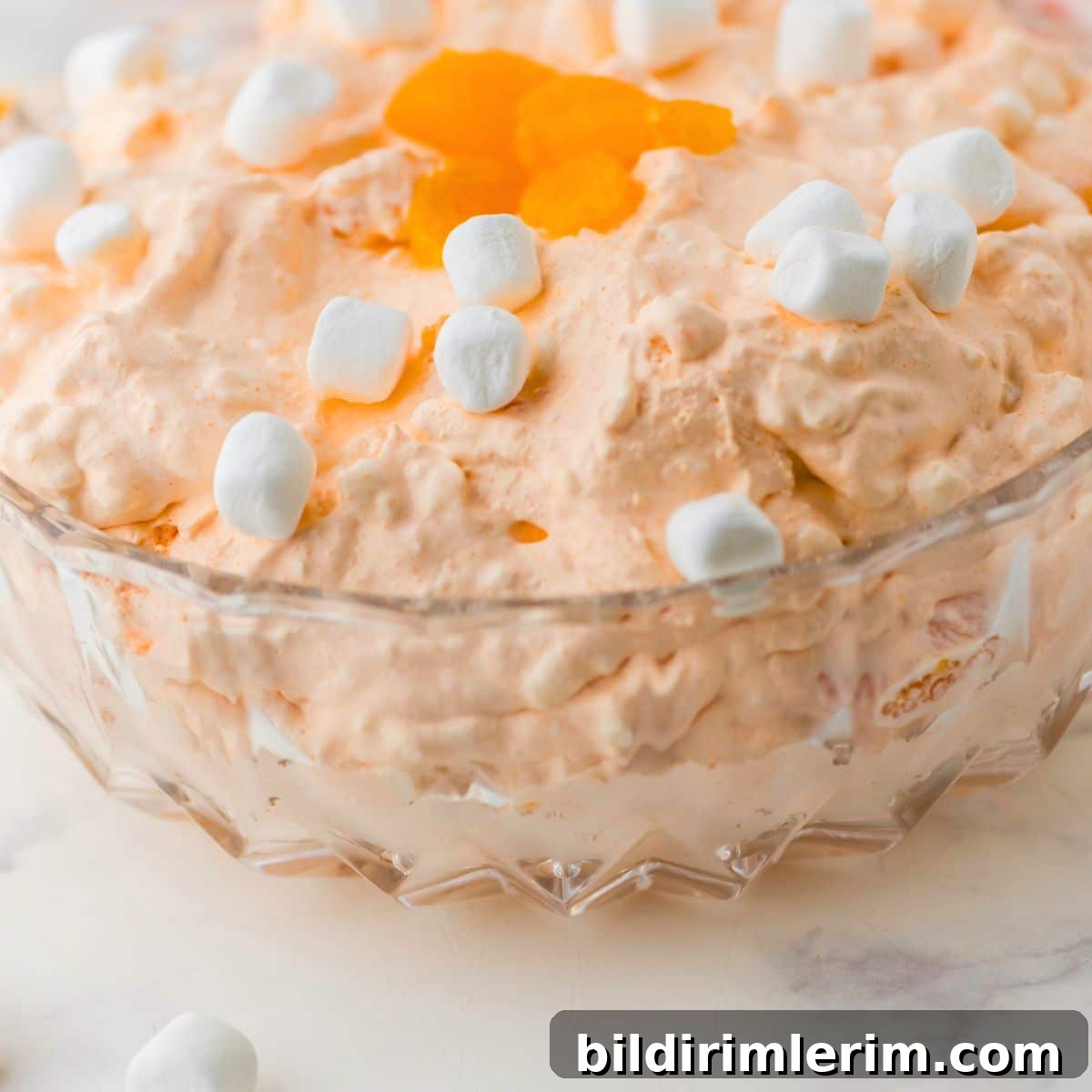 Orange fluff salad in a clear glass serving bowl.
