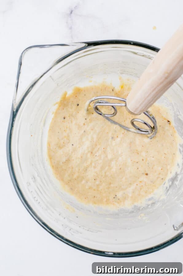 Sourdough discard mixed with spices and oil in a mixing bowl with a danish whisk in it.