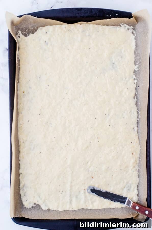 Sourdough discard and spices spread thinly on a parchment lined baking pan for sourdough crackers.