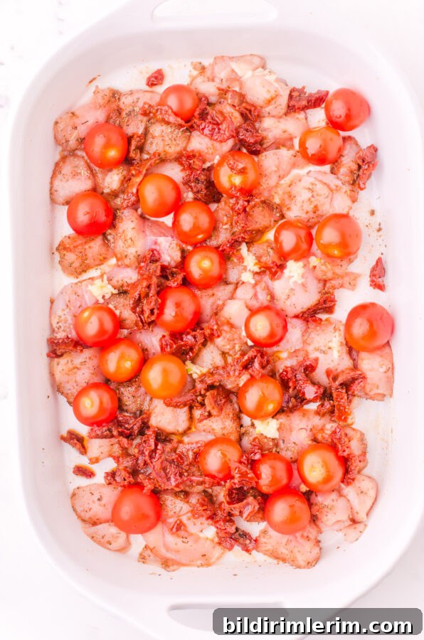 Cherry tomatoes and sundried tomatoes scattered over the top of diced chicken in the baking dish.