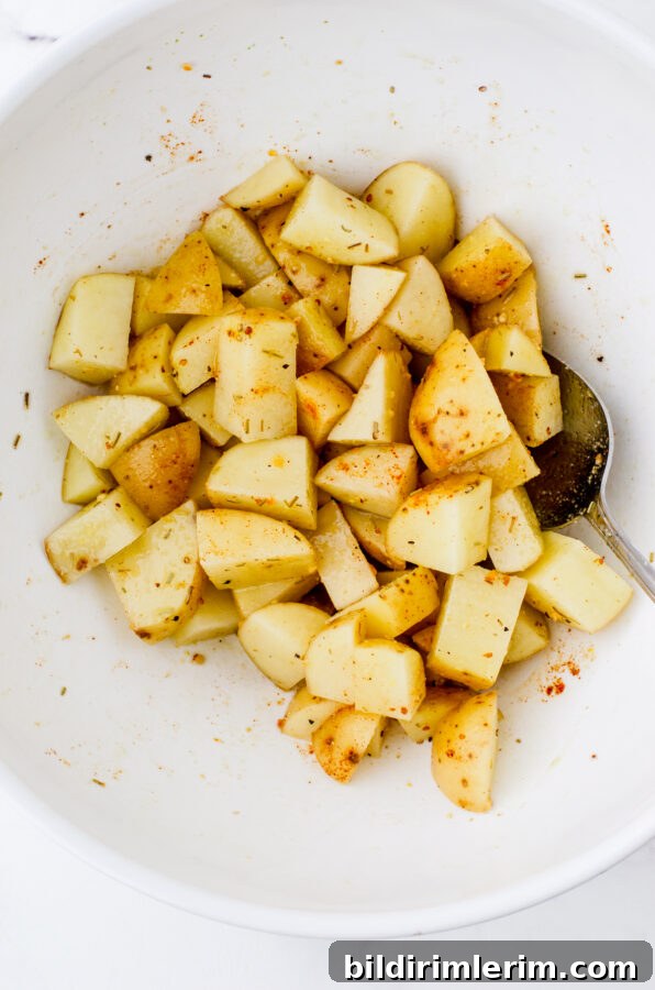 Crispy Oven-Roasted Diced Potatoes Recipe 4 Diced potatoes in a mixing bowl that have been tossed with olive oil and spices.