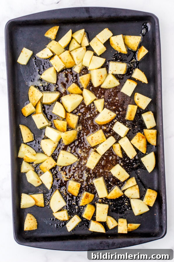 Crispy Oven-Roasted Diced Potatoes Recipe 5 Diced potatoes with olive oil and spices on a stoneware pan ready to be baked