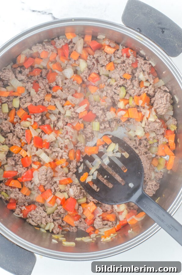 Browned ground beef and sautéed vegetables in a large stockpot for hamburger rice soup.