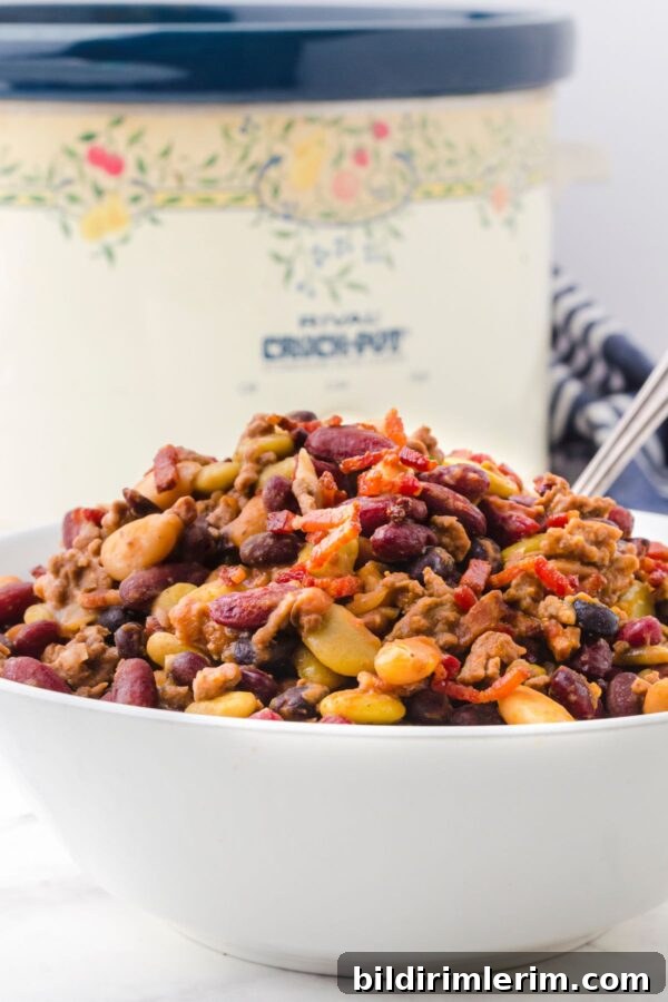 A serving dish full of crock pot baked beans with a crock pot behind it.