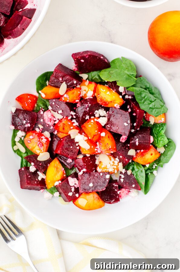 Serving bowl of beet and peach salad on a bed of spinach.